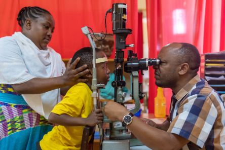Ein Mann schaut durch ein Augenuntersuchungsgerät in die Augen eines Kindes.