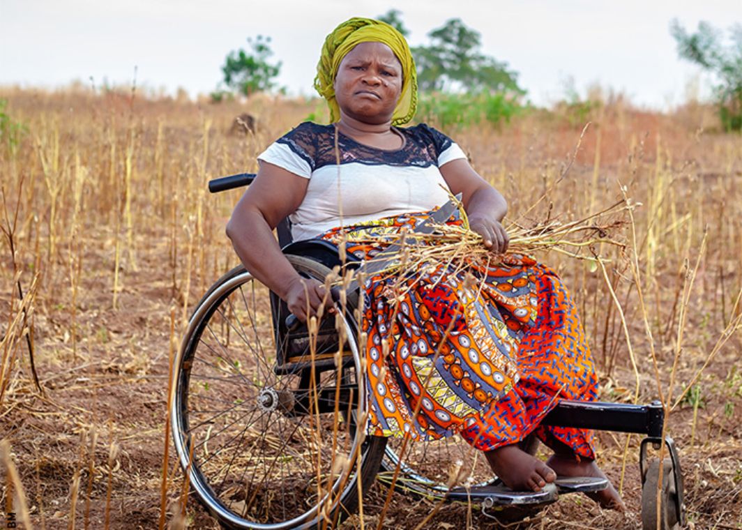 A woman sitting in a wheelchair in dry field. 