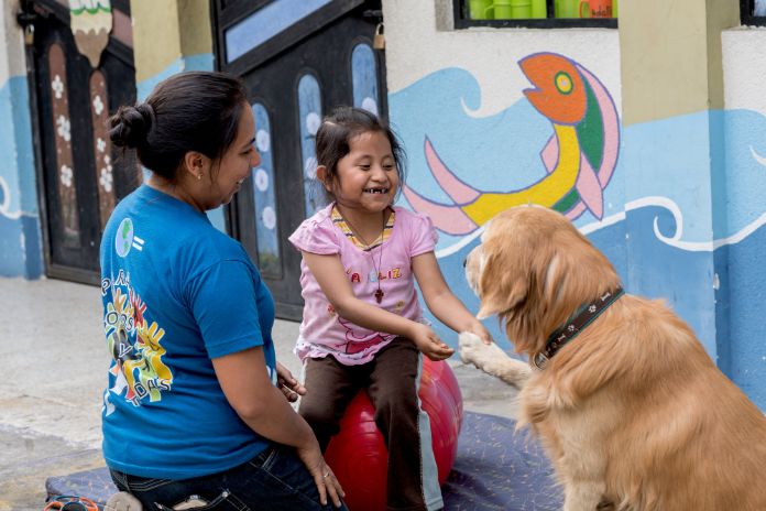 A young girl playing with a dog. A teacher is close by