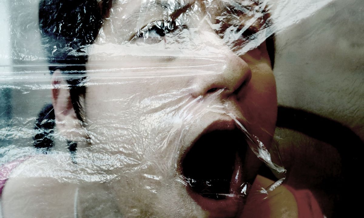 Frauengesicht hinter einer Folie. Es ist unklar, ob sie ihr Gesicht leicht in die Folie drückt oder ob die Folie auf ihr Gesicht gedrückt wird.