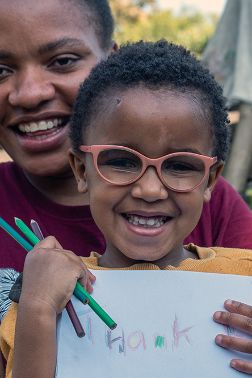 Eine lachende Frau und ein lächelndes Mädchen halten ein Blatt Papier, auf dem &quot;Thank u&quot; steht.