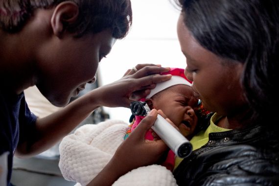 An audio technician screening patient and her 3 months old daughter Jemima. The baby suffers from otitis media.